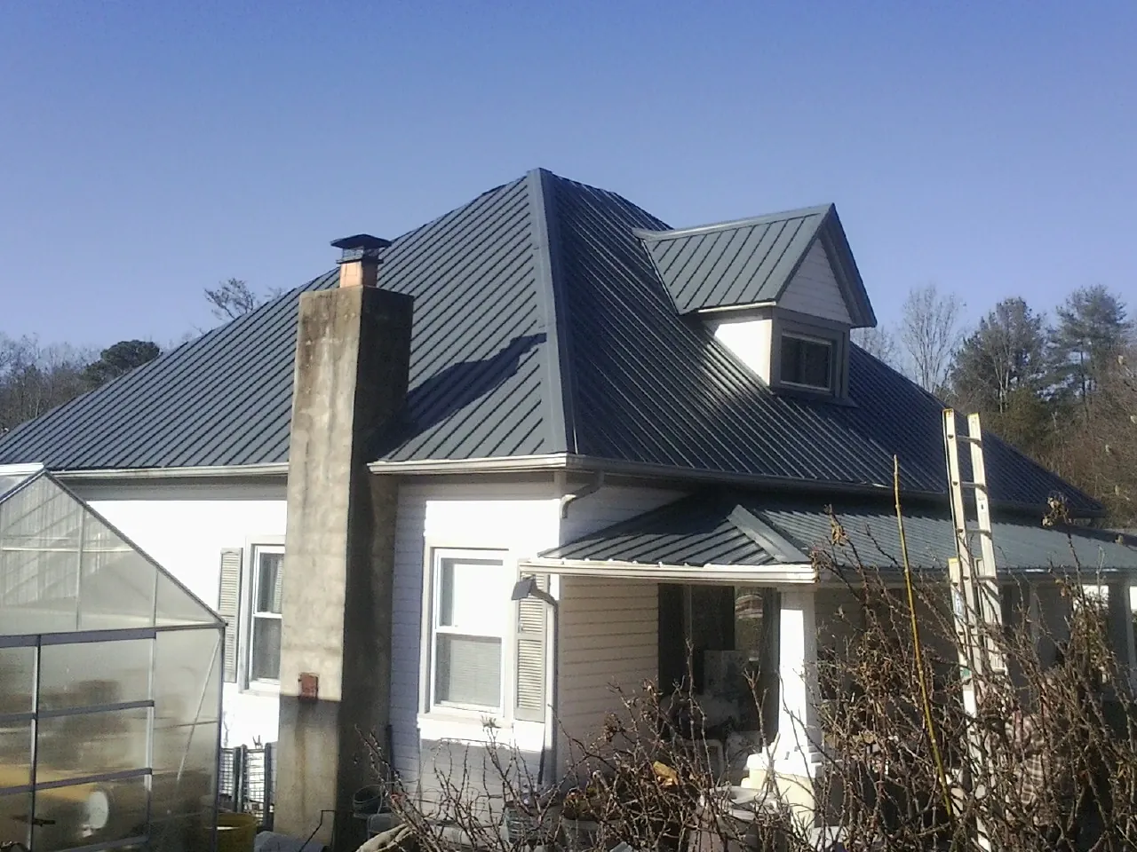 Dark blue standing seam metal roof on a white farmhouse with dormer — Slate & Tile Roof Repair by Roofing Brothers in Kansas City