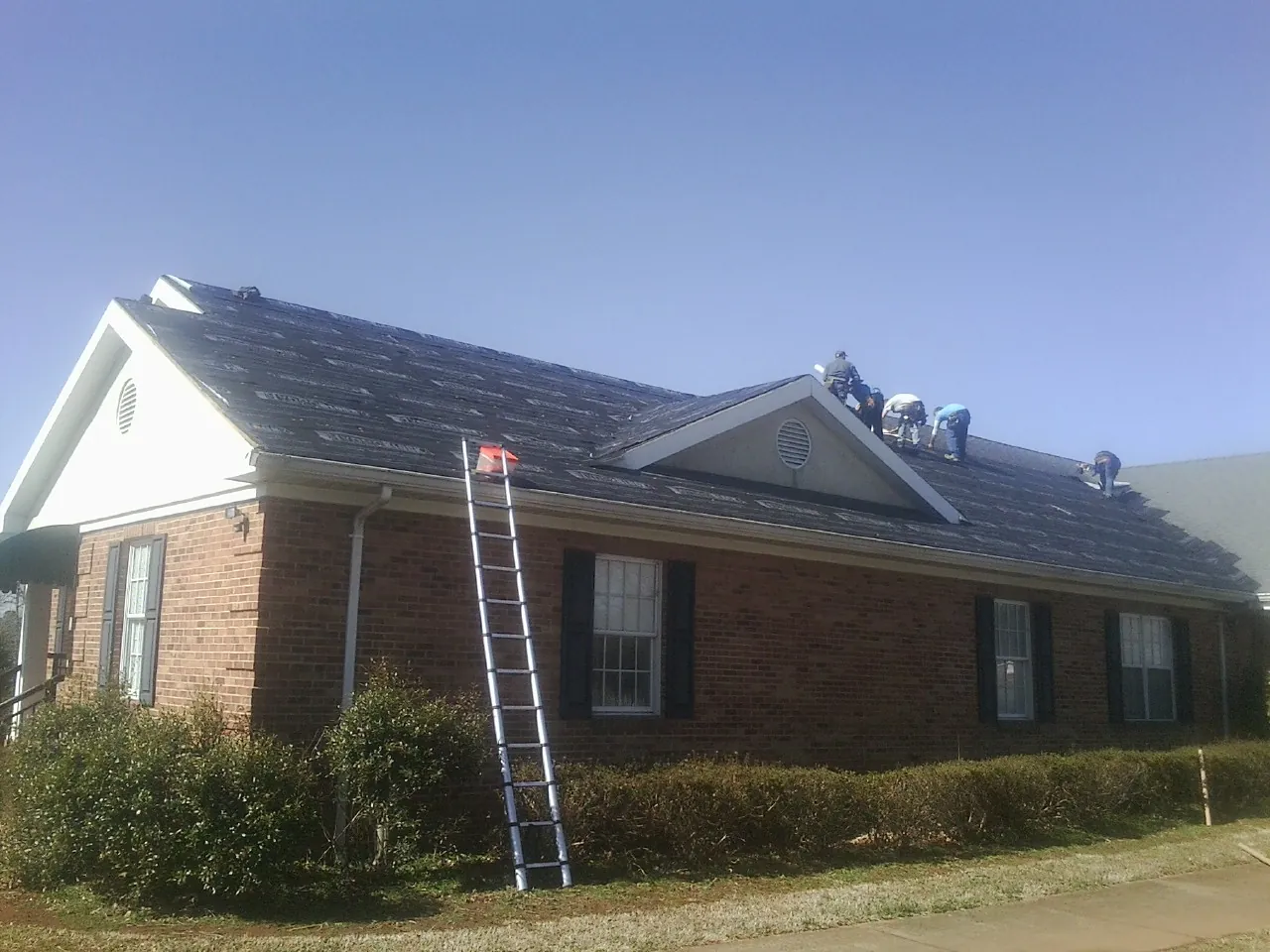 Crew tearing shingles off a brick ranch roof with a ladder set — Emergency Roof Repair work by our crew in Kansas City