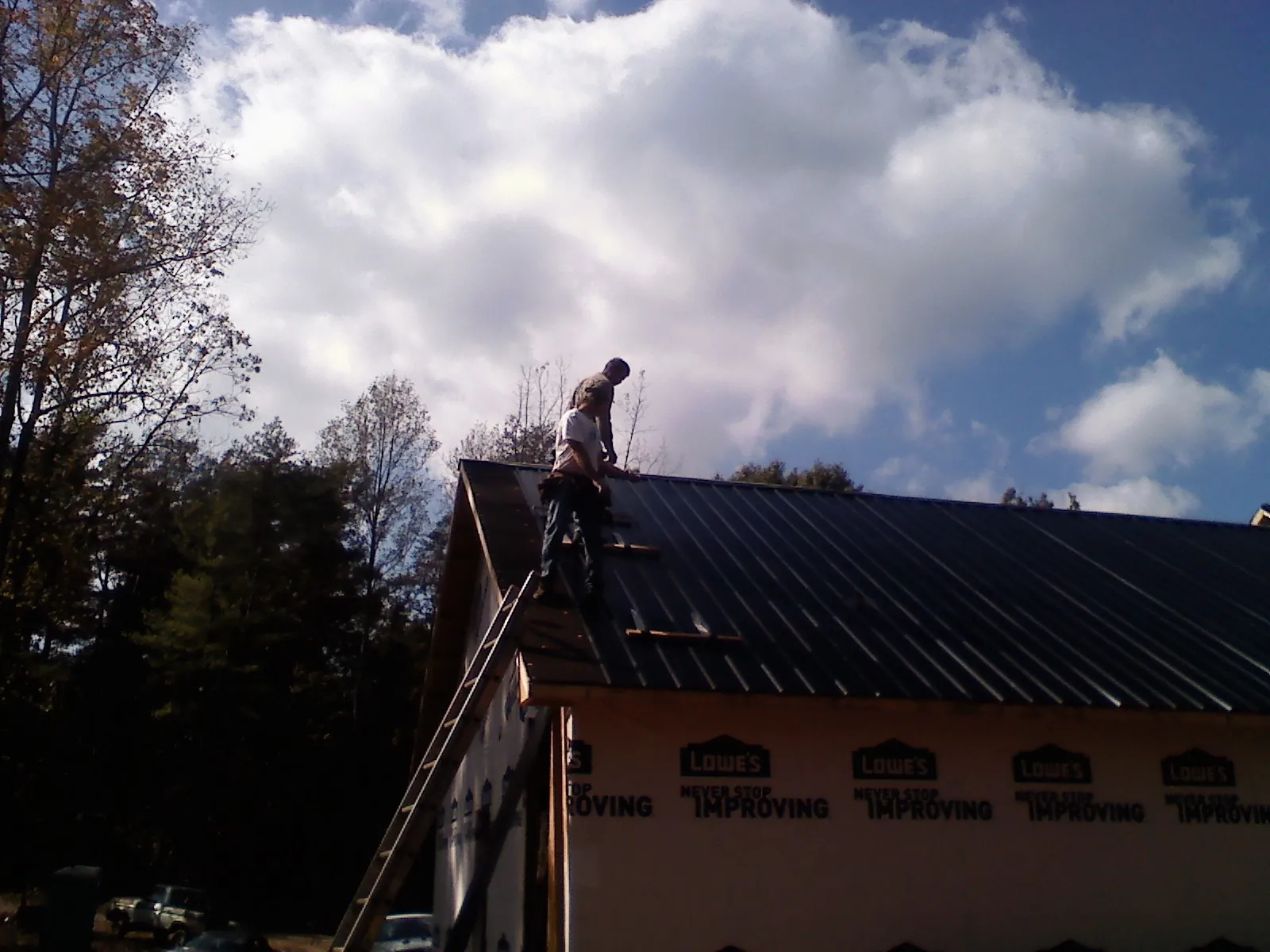 Roofer fastening dark metal panels high against a cloudy sky, from a Roof Inspection job in Kansas City