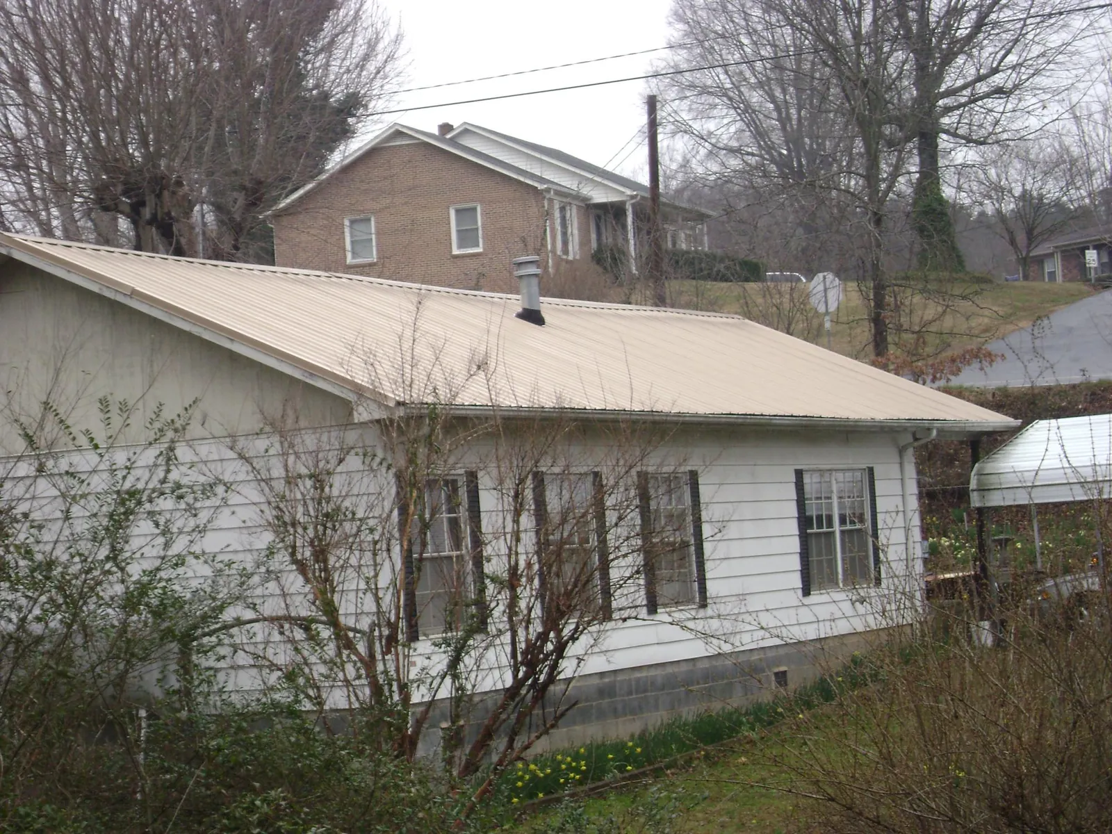 Tan metal roof on a white sided house set into a hillside — Commercial Roofing by Roofing Brothers in Kansas City