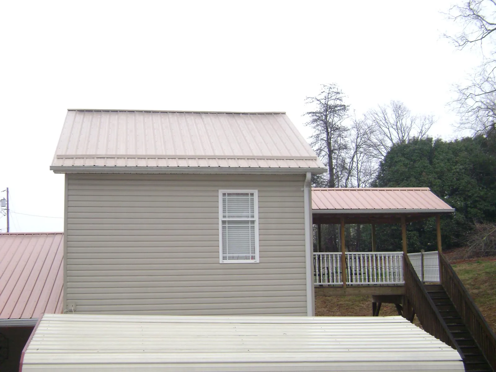 Tan metal roofs on a two story addition and attached porch, from a Roof Replacement job in Kansas City
